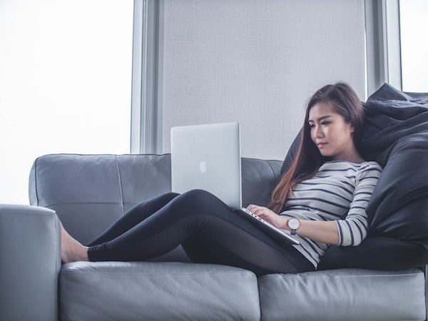 remote worker with Apple laptop sitting on gray couch